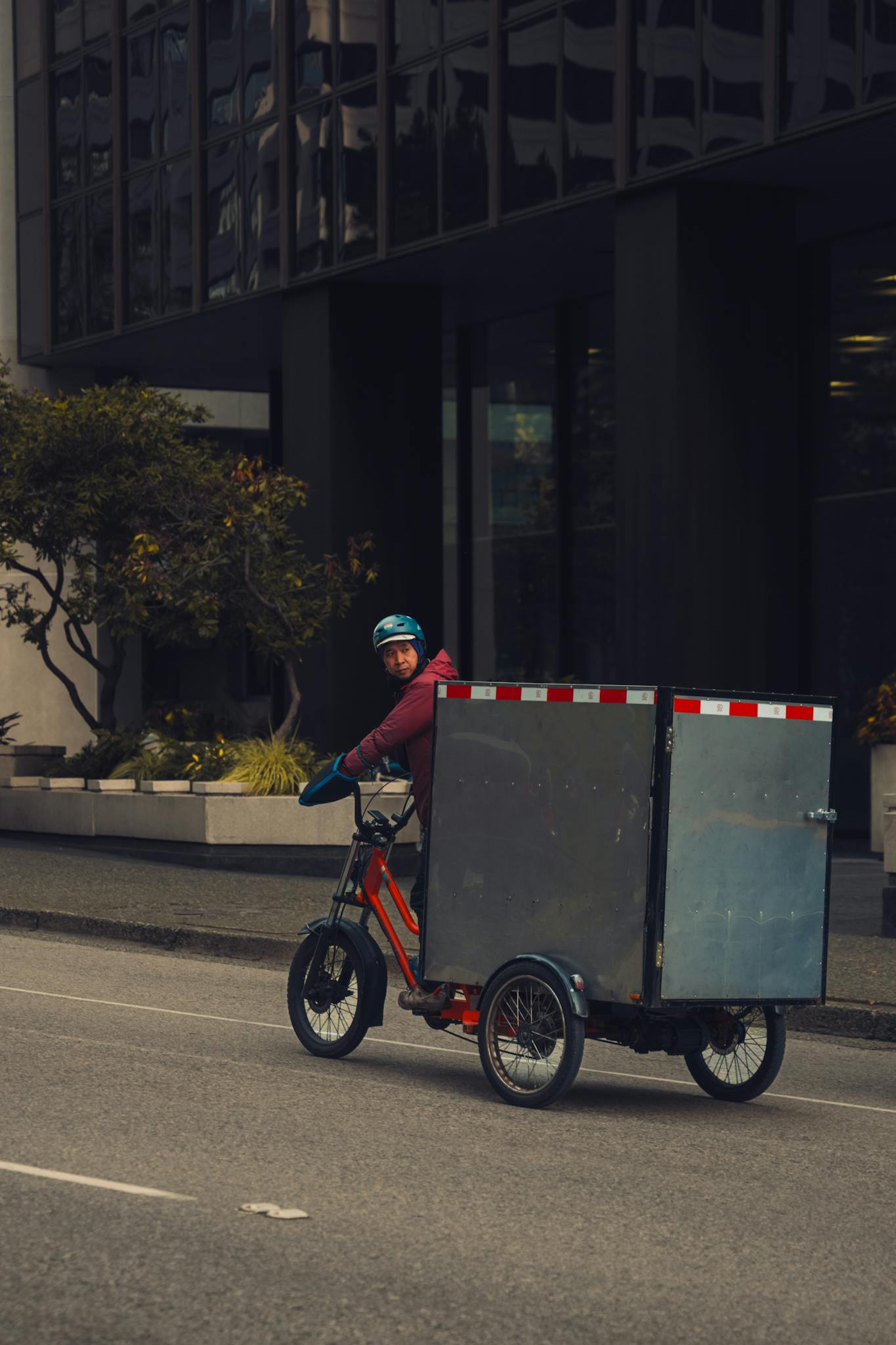 A delivery person rides a tricycle with a large box on an urban street, showcasing sustainable city transport.